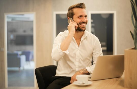 smiling formal male with laptop chatting via phone